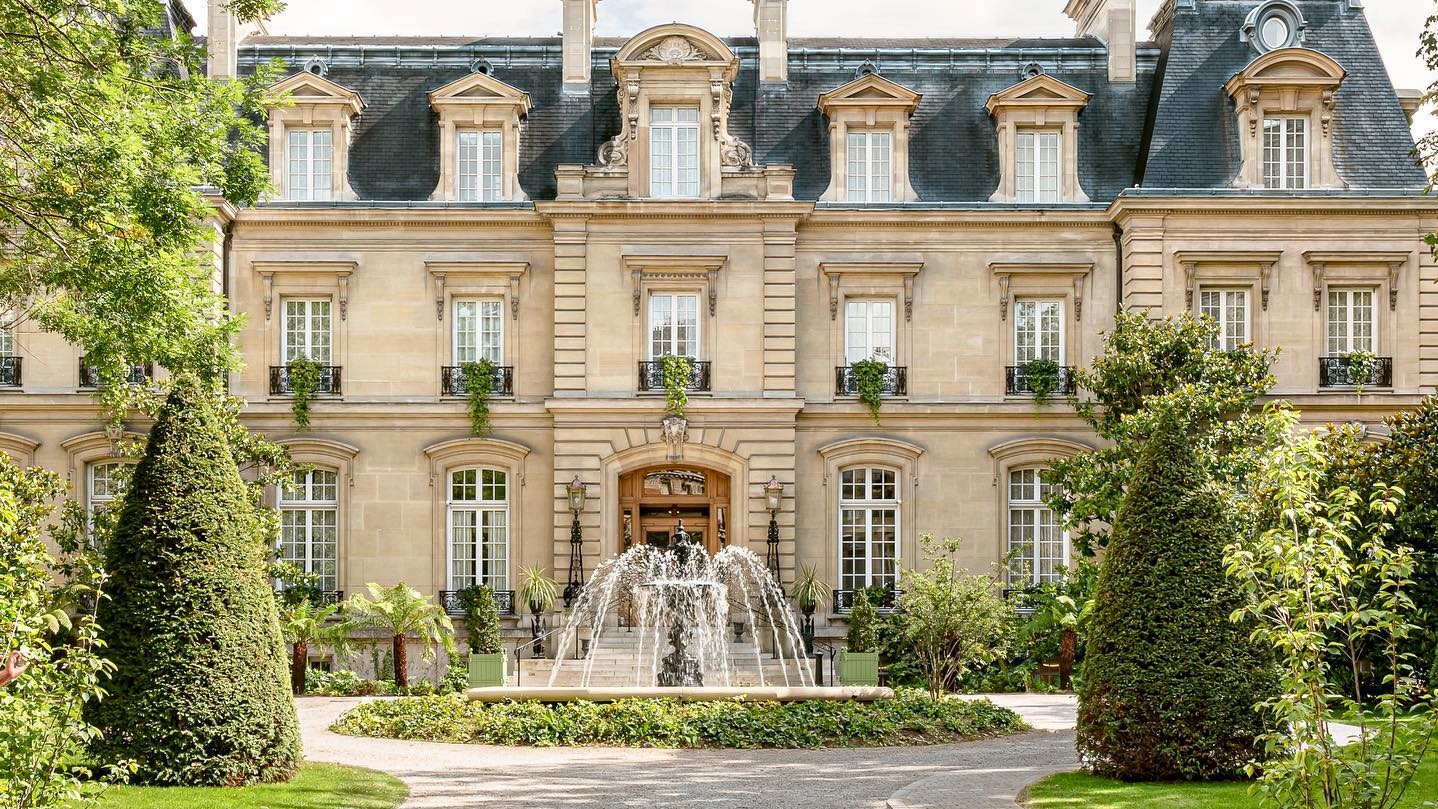 Outside of saint james paris with a fountain infront of the main entrance surrounded by plants and trees