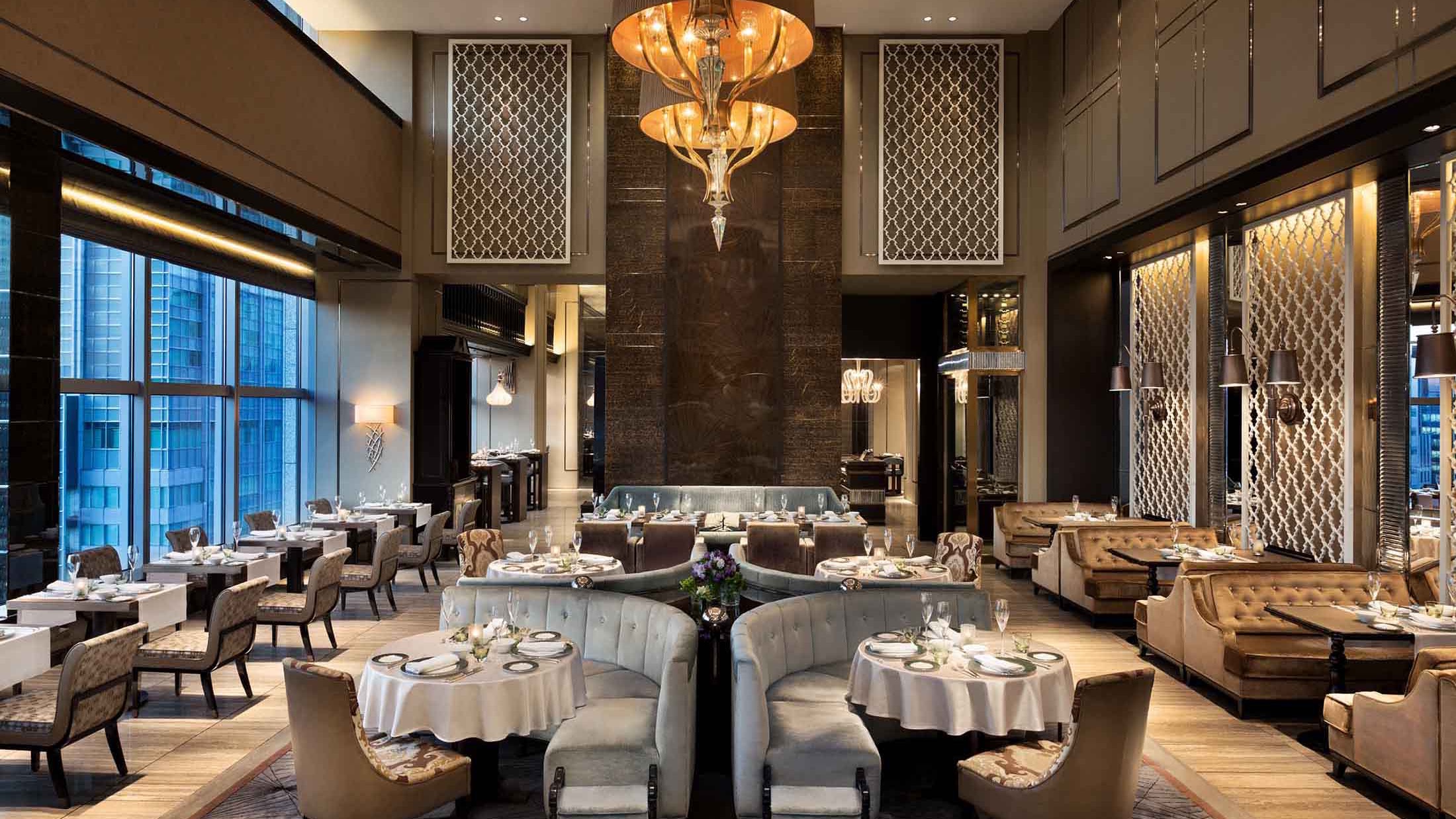 Dining area with grey decor sofas and beige design chairs, marble walls, large golden lamp and windows to the city.