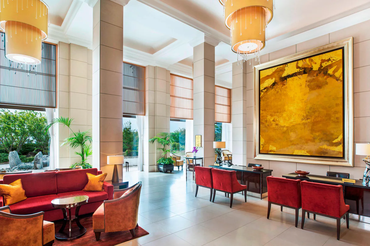 Dining area with red chair, sofas, white floor, yellow painting and windows to nature at The St. Regis Osaka.