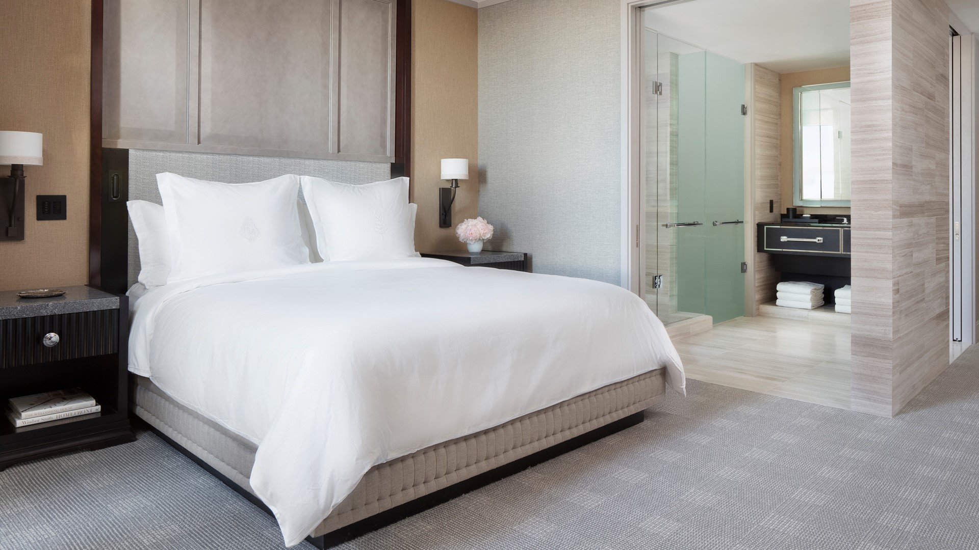 Hotel suite with a king sized bed, grey carpet and a bathroom on the left side.