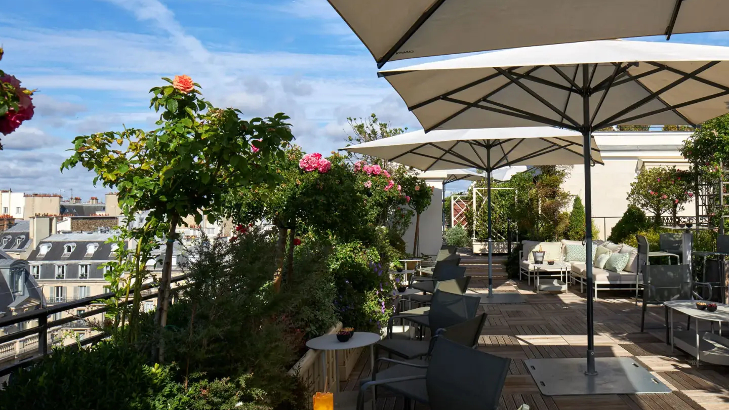 Rooftop with plants, white and grey furniture, wooden floor, and view of Paris at Le Rooftop at Hotel Raphael.