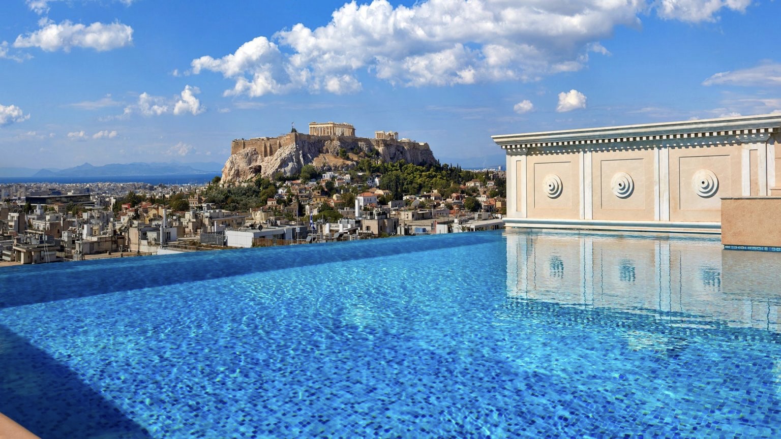 Infinity pool with clear blue water, and a insane view of nature, the city of Athens and a ancient building on top of mountain.