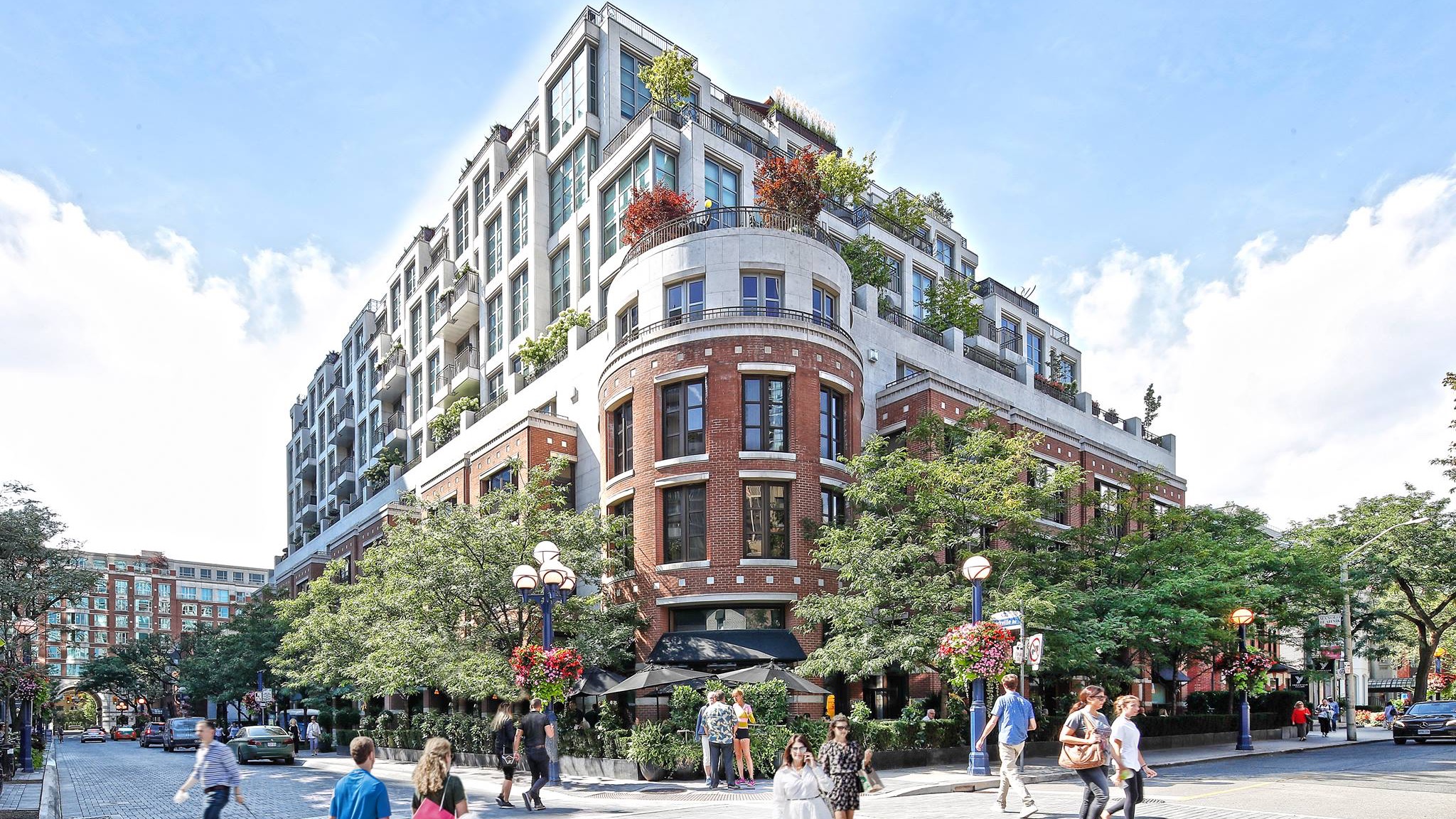 The outside of the hazelton hotel toronto made of brick and glass windows with people walking on the street